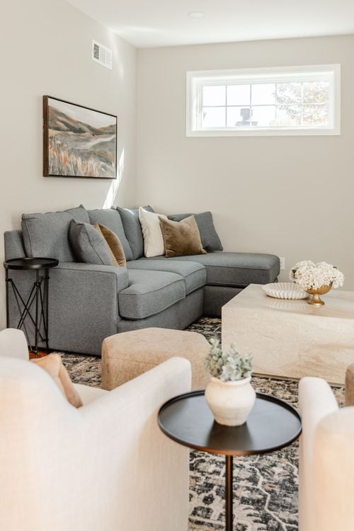 Living room with a charcoal gray sectional, landscape art and a marble coffee table