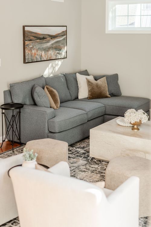 Living room corner with a charcoal gray sectional, landscape painting and stone coffee table