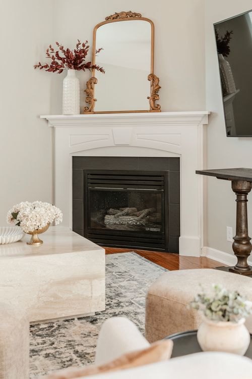 White mantel fireplace with an ornate gold mirror, dried florals and marble coffee table