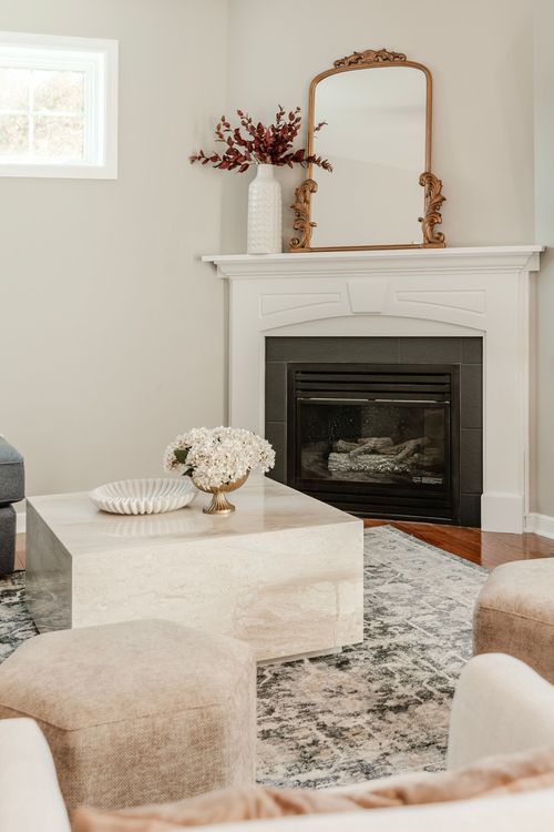 Corner fireplace with a gold mirror, white vase and stone coffee table topped with hydrangeas
