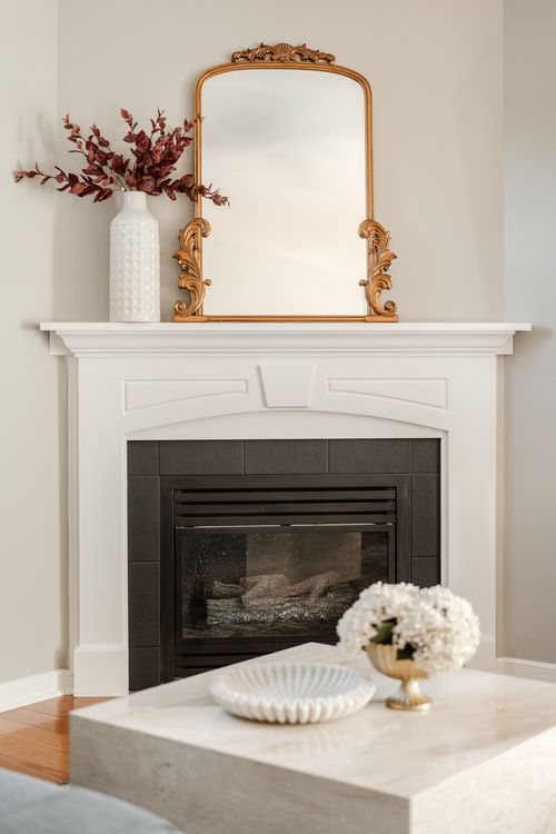 White mantel fireplace with an ornate gold mirror, dried florals and a marble coffee table