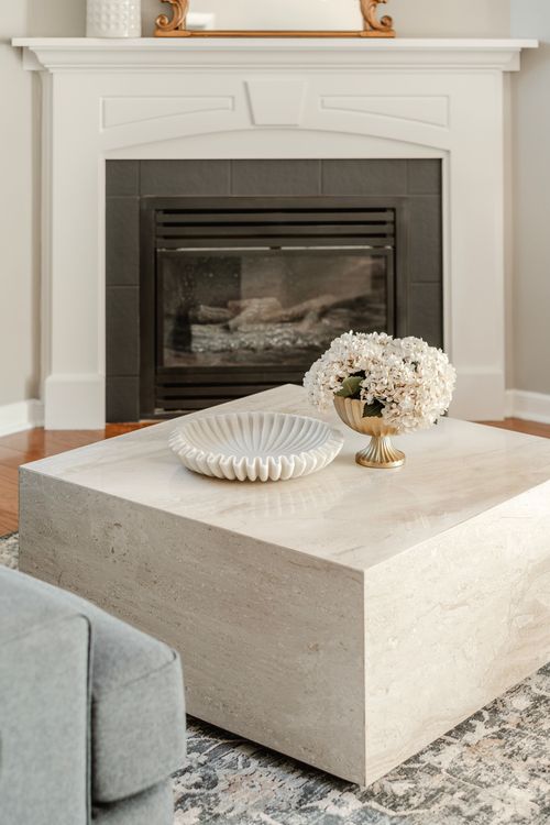 Marble coffee table styled with a scalloped bowl and hydrangeas beside a lit fireplace