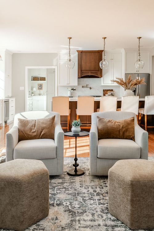 Open kitchen with glass pendant lights, wood range hood and cream swivel chairs in view