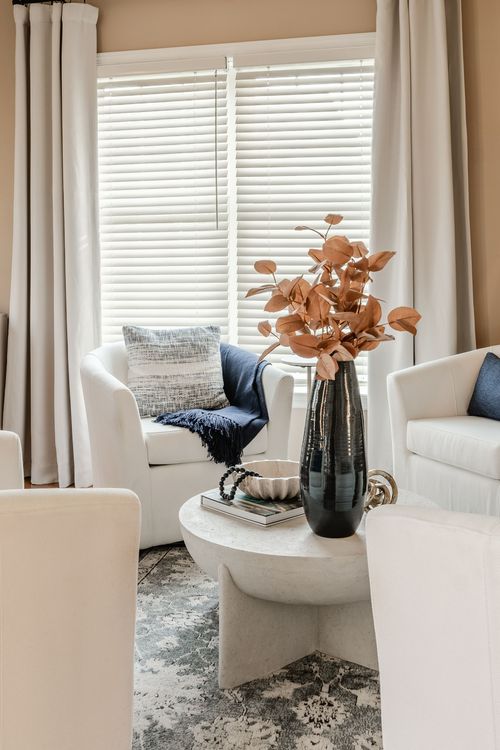 Sitting nook with white swivel chairs, blue accent pillows and dried florals in a black vase