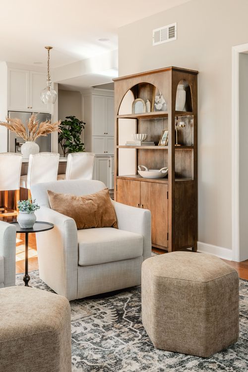Sitting area with a gray swivel chair, wood arched bookshelf and a view into the kitchen