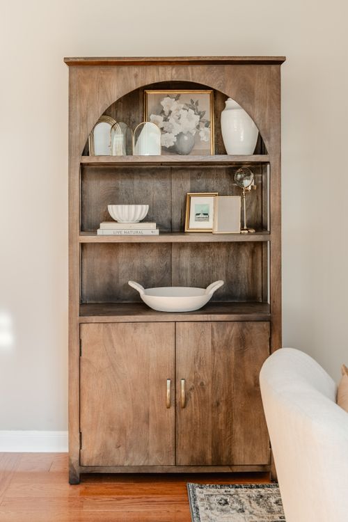 Wood arched bookshelf styled with framed art, ceramic vases and a glass finial