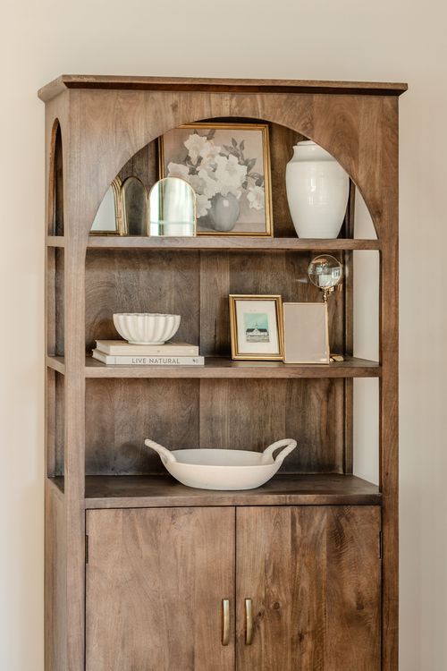 Close-up of a wood arched bookshelf with framed floral art, a globe and ceramic bowls