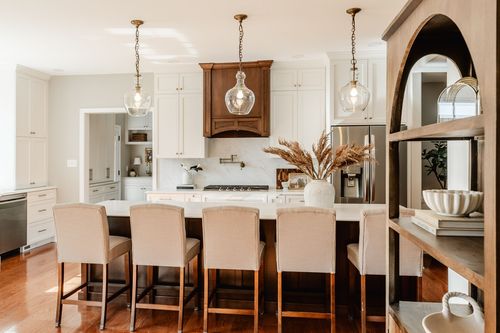 Kitchen with glass pendant lights, a dark wood range hood and neutral upholstered barstools