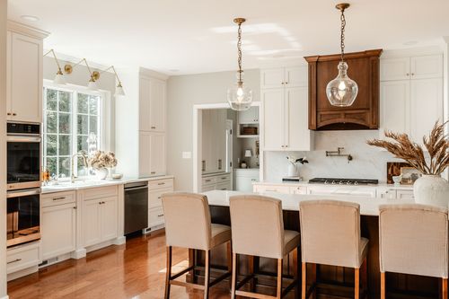 Kitchen with white cabinetry, brass sconces, dried pampas grass and cream barstools
