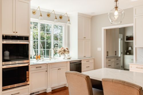 Kitchen sink window with triple brass sconce lighting and stacked wall ovens