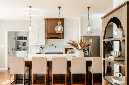 Kitchen island with glass pendant lights, a wood range hood and marble backsplash