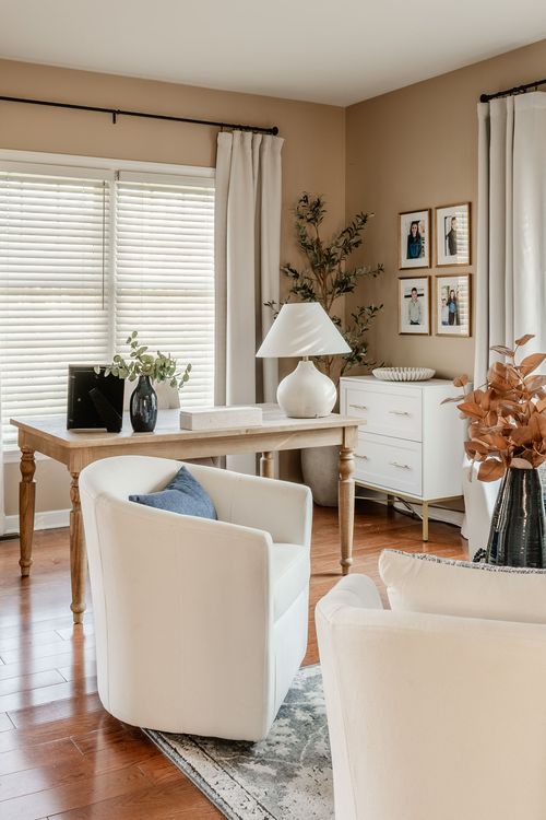 Home office desk with a white pedestal lamp, family photo gallery wall and white dresser