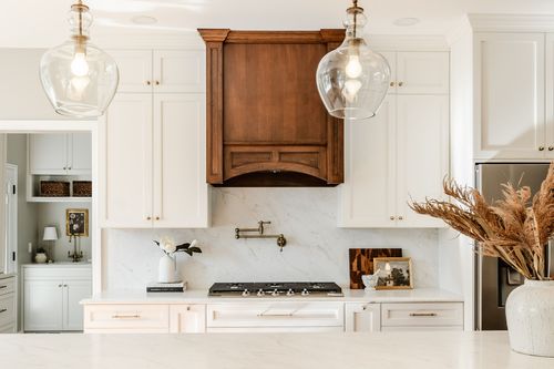 Kitchen range with a carved wood hood, marble backsplash and glass pendant lighting