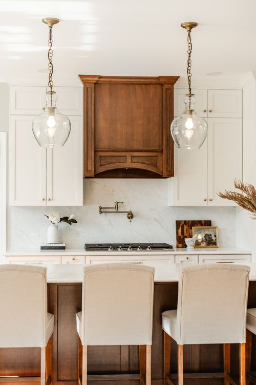 Kitchen island seating with a wood range hood, glass pendants and cream upholstered barstools