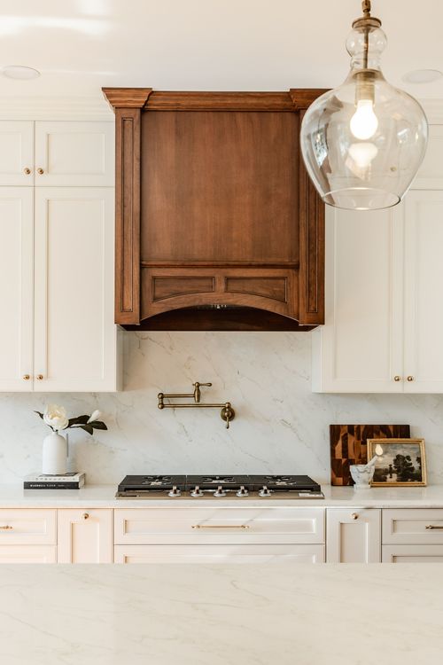 Wood carved range hood with a brass pot filler faucet over a marble backsplash