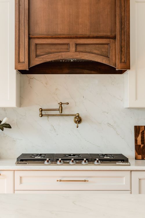 Close-up of a carved wood range hood, brass pot filler and gas cooktop