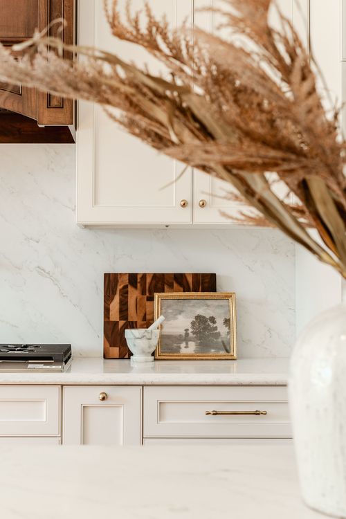 White cabinets with wood cutting boards, framed art print and dried pampas grass on a marble counter