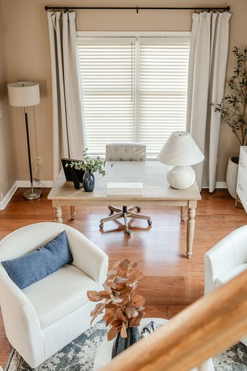 Home office with a wood desk, white tufted chair and a view into a sitting area