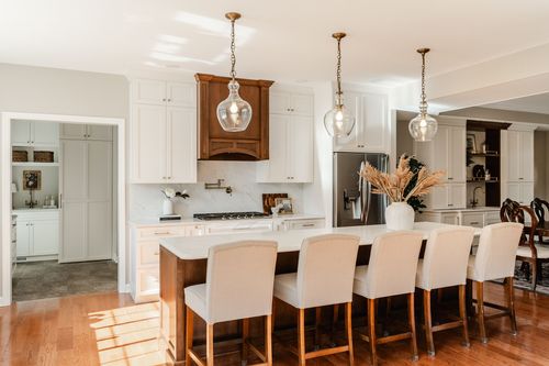 Kitchen with dark wood island seating, cream upholstered chairs and three glass pendant lights