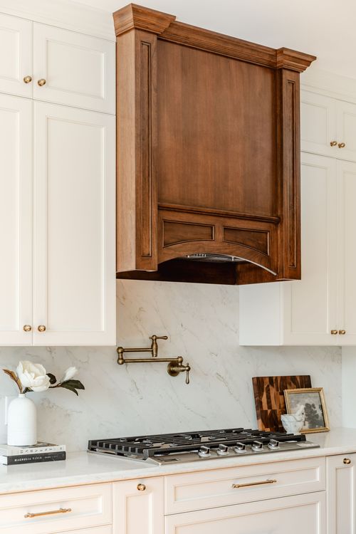 Arched dark wood range hood with brass pot filler over a marble backsplash and stainless cooktop