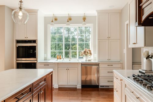 Kitchen with white cabinetry, brass wall sconces over the window and a stainless wall oven