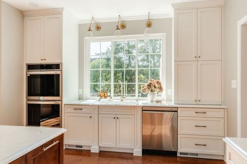 White kitchen with stacked stainless wall ovens, brass sconces and marble countertops