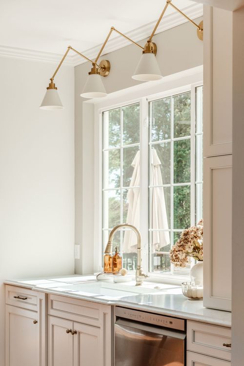 Kitchen sink nook with brass swing-arm sconces, marble counters and a gold gooseneck faucet