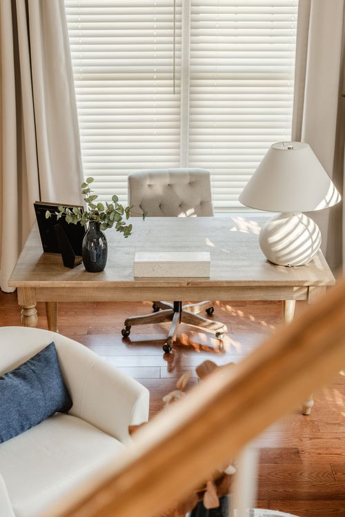 Wood desk detail with a tufted gray office chair, table lamp and framed family photo