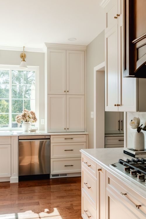 Tall white pantry cabinetry beside a stainless dishwasher and a sunlit window