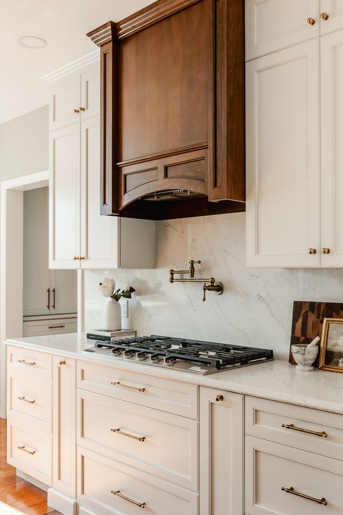 Dark wood range hood above a gas cooktop flanked by white cabinets and a marble backsplash