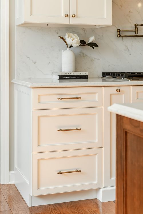 Cream cabinet drawers with brass bar pulls beneath a white marble countertop