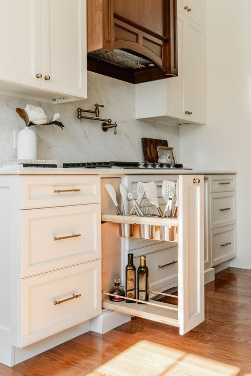 Pull-out kitchen organizer with utensil crocks and oil bottles beside a gas cooktop