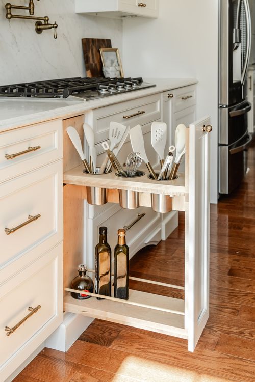Close-up of a wood pull-out drawer holding cooking utensils and olive oil bottles