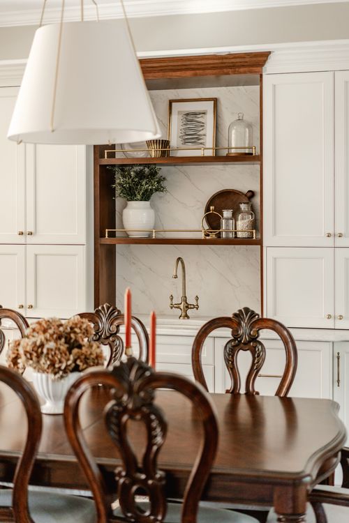 Dining room with carved wood chairs, a candlelit table and open shelving styled with glass jars and art