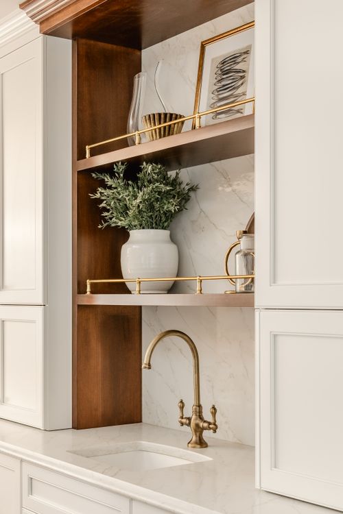 Built-in wood shelving with framed art, glass decanters and brass display rails