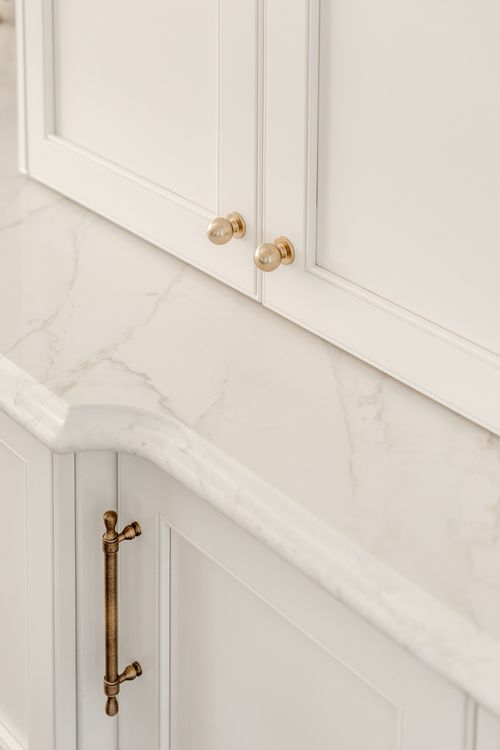 Detail of brass cabinet knobs and a marble countertop edge in a white kitchen