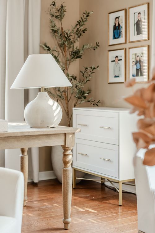 Desk corner with a white ceramic lamp, faux olive tree and white two-drawer nightstand