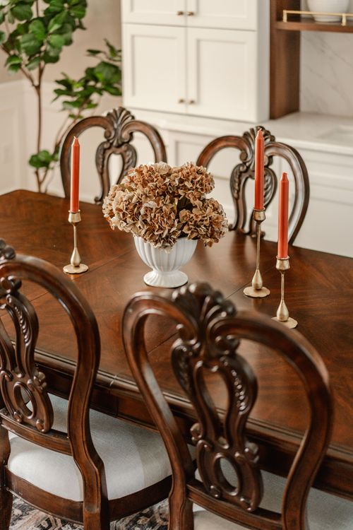 Dining table detail with brass candlesticks, orange tapers and a dried floral centerpiece
