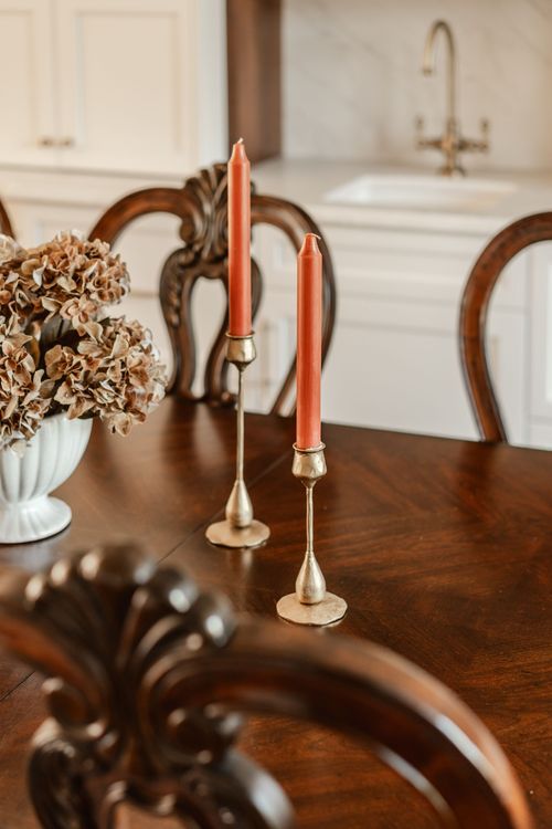 Taper candles in brass holders on a dark wood dining table with a dried hydrangea centerpiece