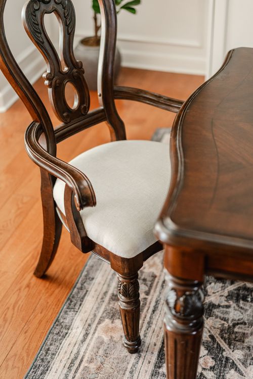 Carved wood dining chair with a cream linen seat beside a patterned area rug