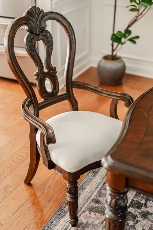 Ornately carved wood armchair with a cream cushion and a potted fig tree nearby