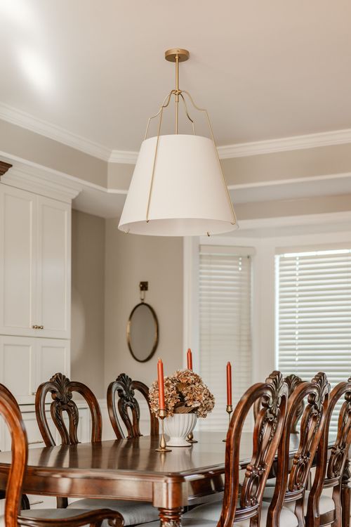 White drum pendant light illuminating a dining room with a round wall mirror