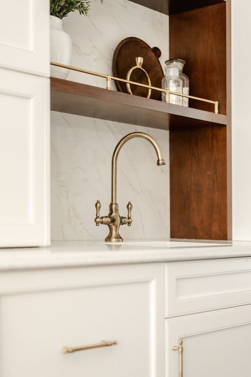 Bar sink with a brass gooseneck faucet beneath wood shelving holding a decanter and glass jars