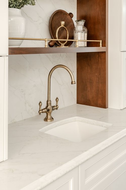 Marble bar sink and brass faucet framed by dark wood shelving and a tile backsplash