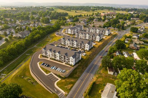 Aerial view of an apartment complex with a curving entrance drive and distant hills