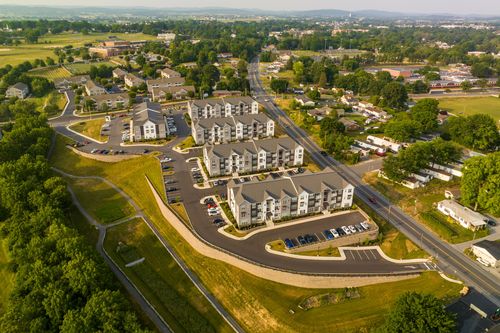 Aerial view of a curving apartment complex driveway with a grassy retention basin alongside