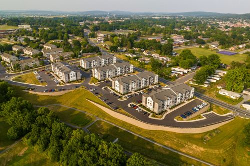 Aerial view of an apartment complex with landscaped parking loops and a town park in the distance