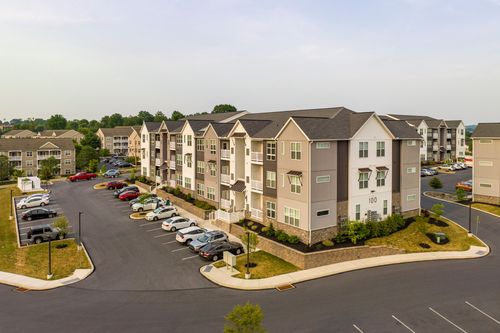 Low aerial view of a tan and brown apartment building with private balconies and parking below
