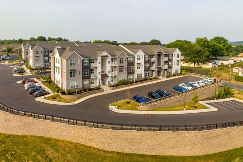 Aerial view of an apartment building with a curved stone retaining wall and rows of parked cars