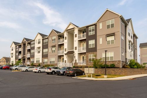 Street-level view of a three-story apartment building with balconies and a landscaped parking lot
